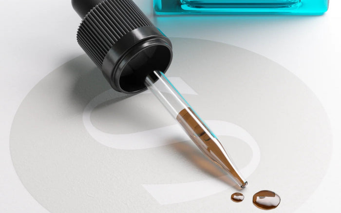 A Superoom glass dropper releasing amber liquid extract onto a white surface, Chaga bottle behind